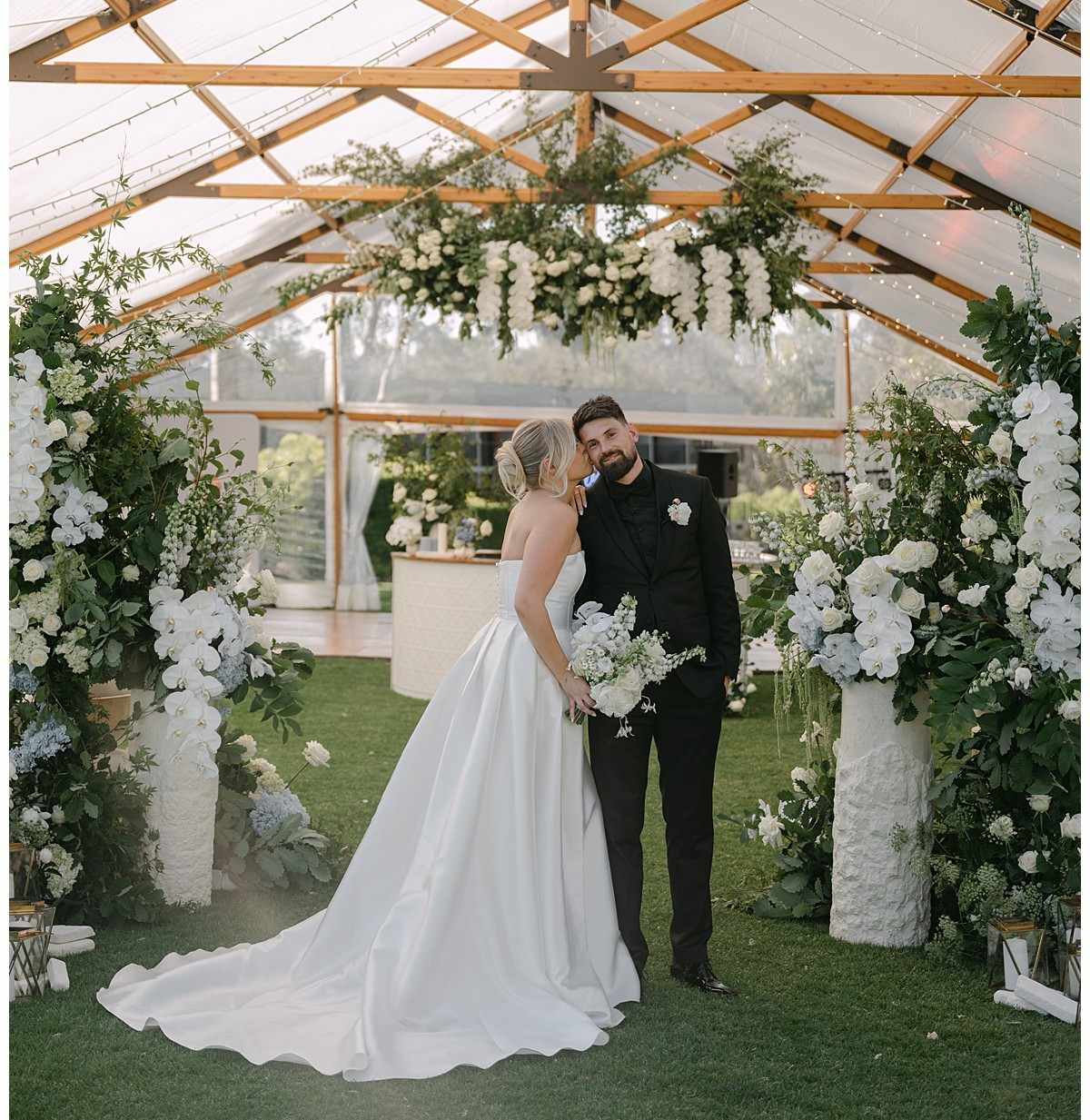 Bride and groom under a white floral wedding installation