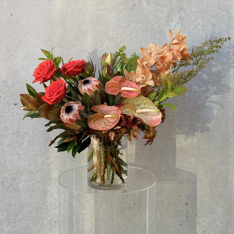 Pastel floral bouquet with orange Anthuriums in a small glass vase
