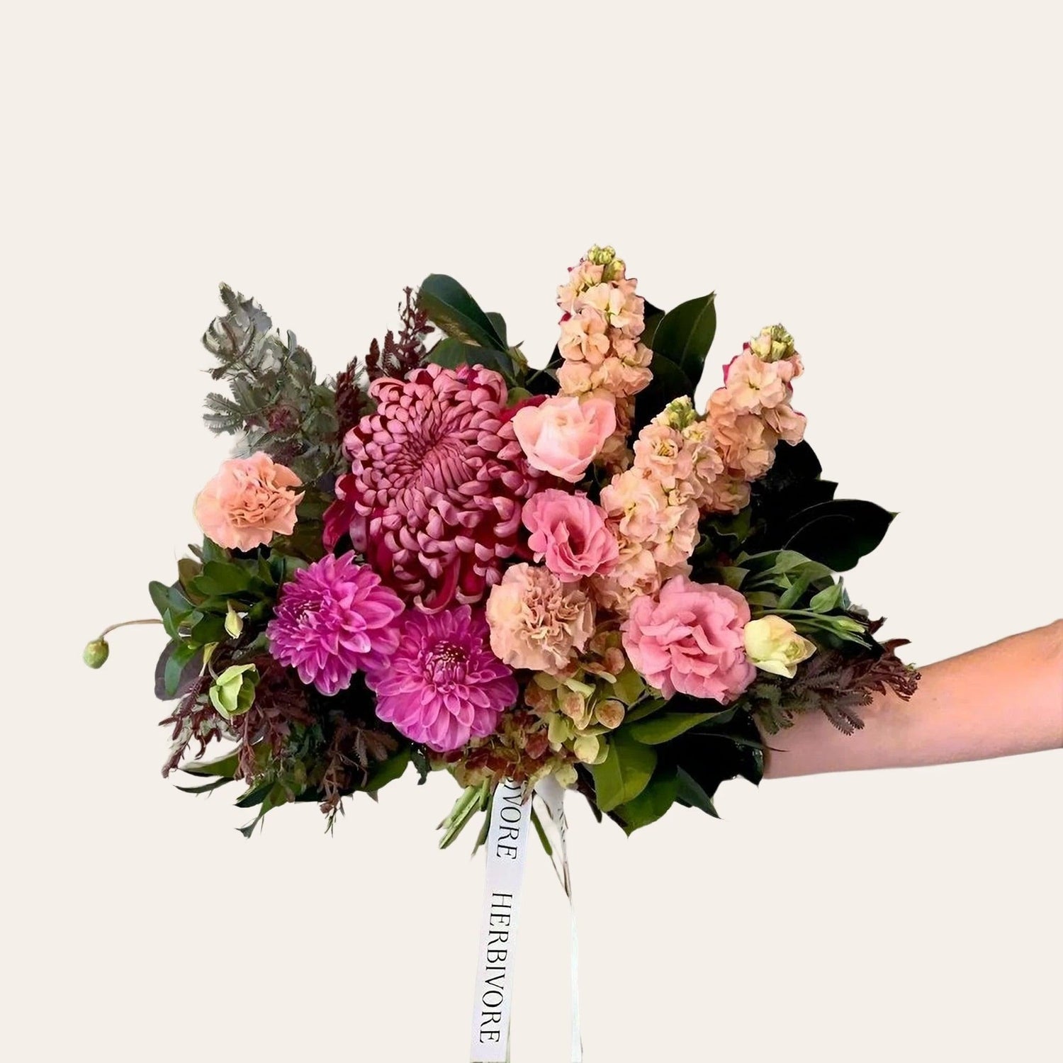 Small bouquet with purple roses, lilies and baby's breath wrapped and tied with ribbon and held by a Herbivore staff member.