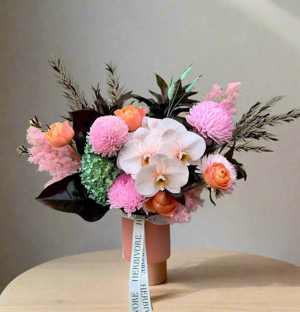 bright pink flower bouquet with pink disbuds, orange roses and preserved hydrangea in a pink vase