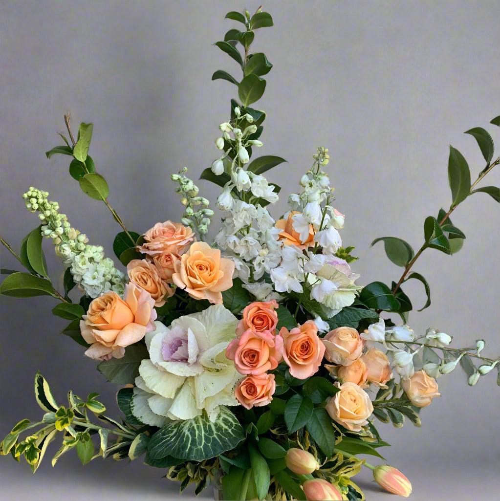 Elegant floral arrangement titled 'Peachy Love' featuring peach roses, white blooms, and lush greenery