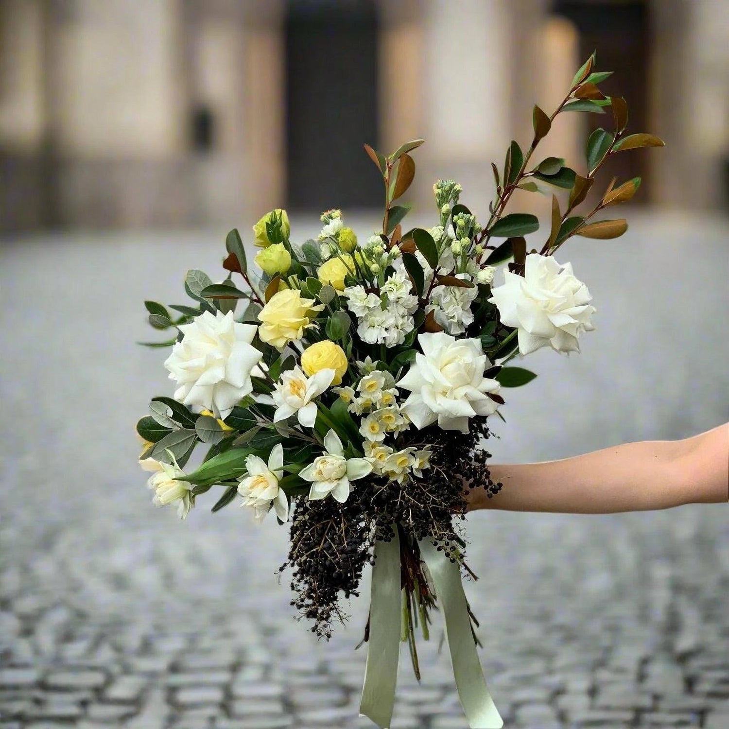 Elegant floral bouquet with white roses and green foliage held in a bouquet tied together by a Herbivore staff member