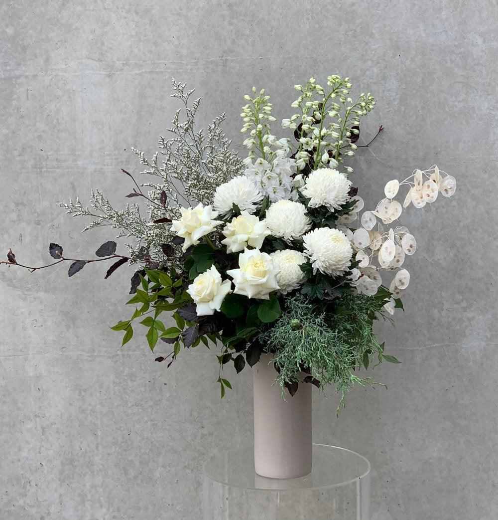 white themed bouquet with white roses, white disbuds and some simple green foliage in a beige vase.