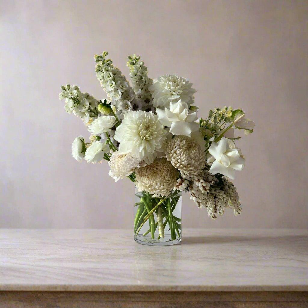 Small white arrangement with white roses, baby's breath and white disbuds in a glass vase