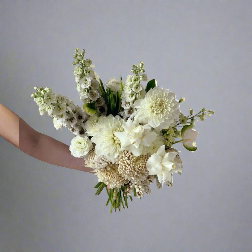 Small white arrangement with white roses, in a small posy being held by one of Herbivore's florists