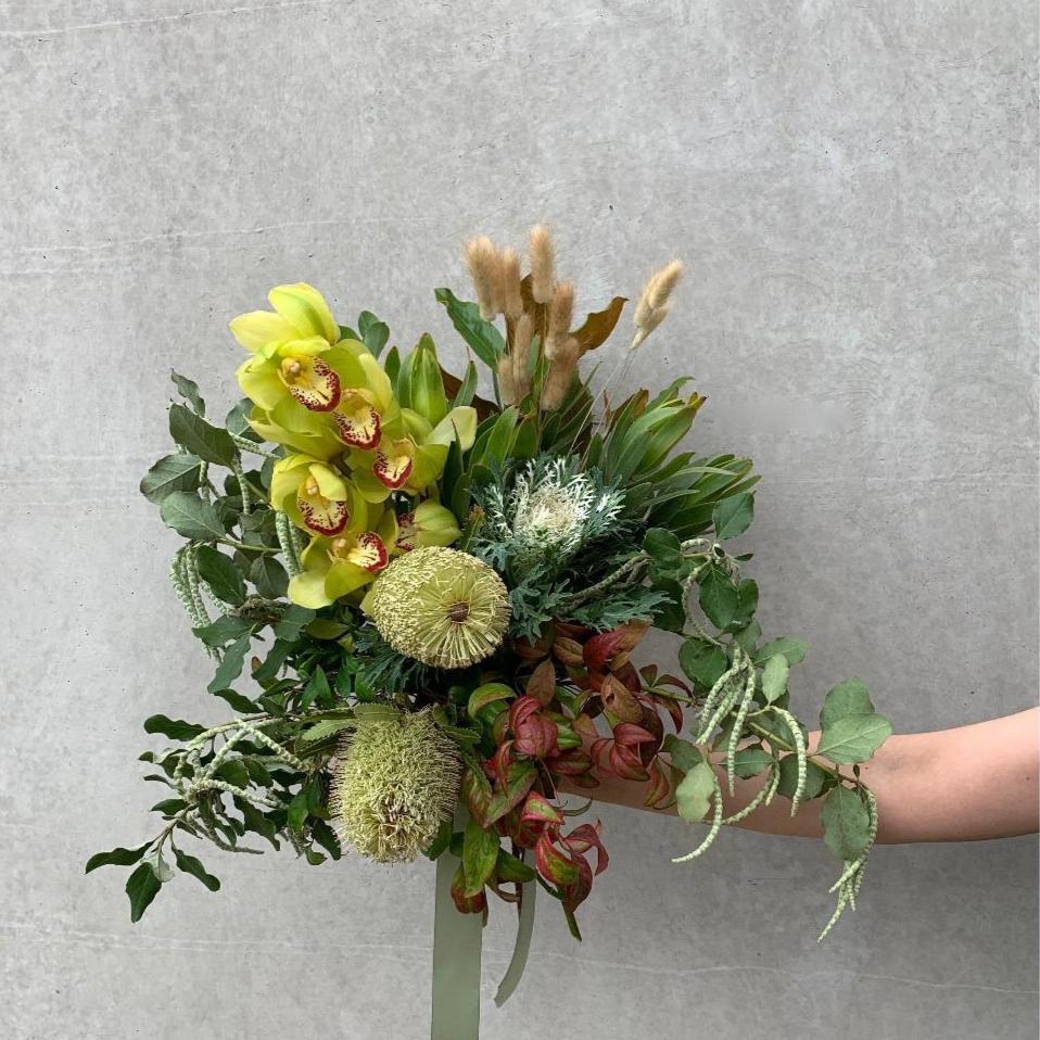 Florist arrangement with native flowers like banksias in a small bouquet being held by a Herbivore staff member.