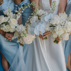 Bridesmaids in light blue satin dresses holding white and pale blue flower bouquets beside a bride in a white satin wedding gown.