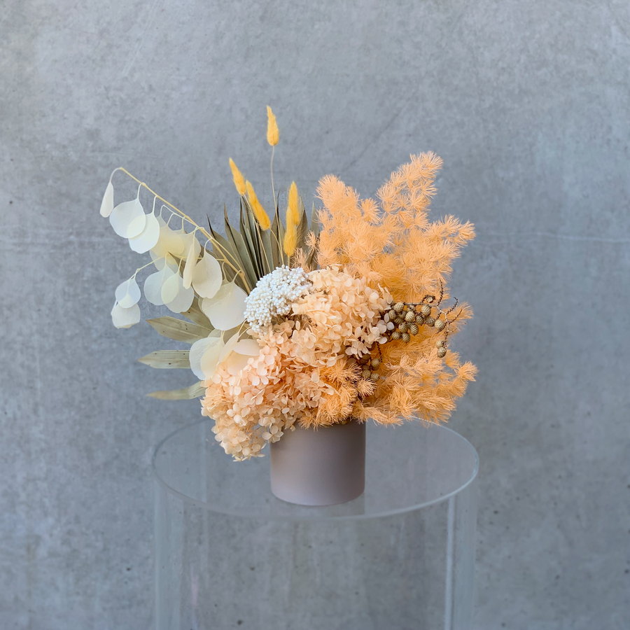 A preserved flower arrangement in natural & peach tones displayed in a grey vase.