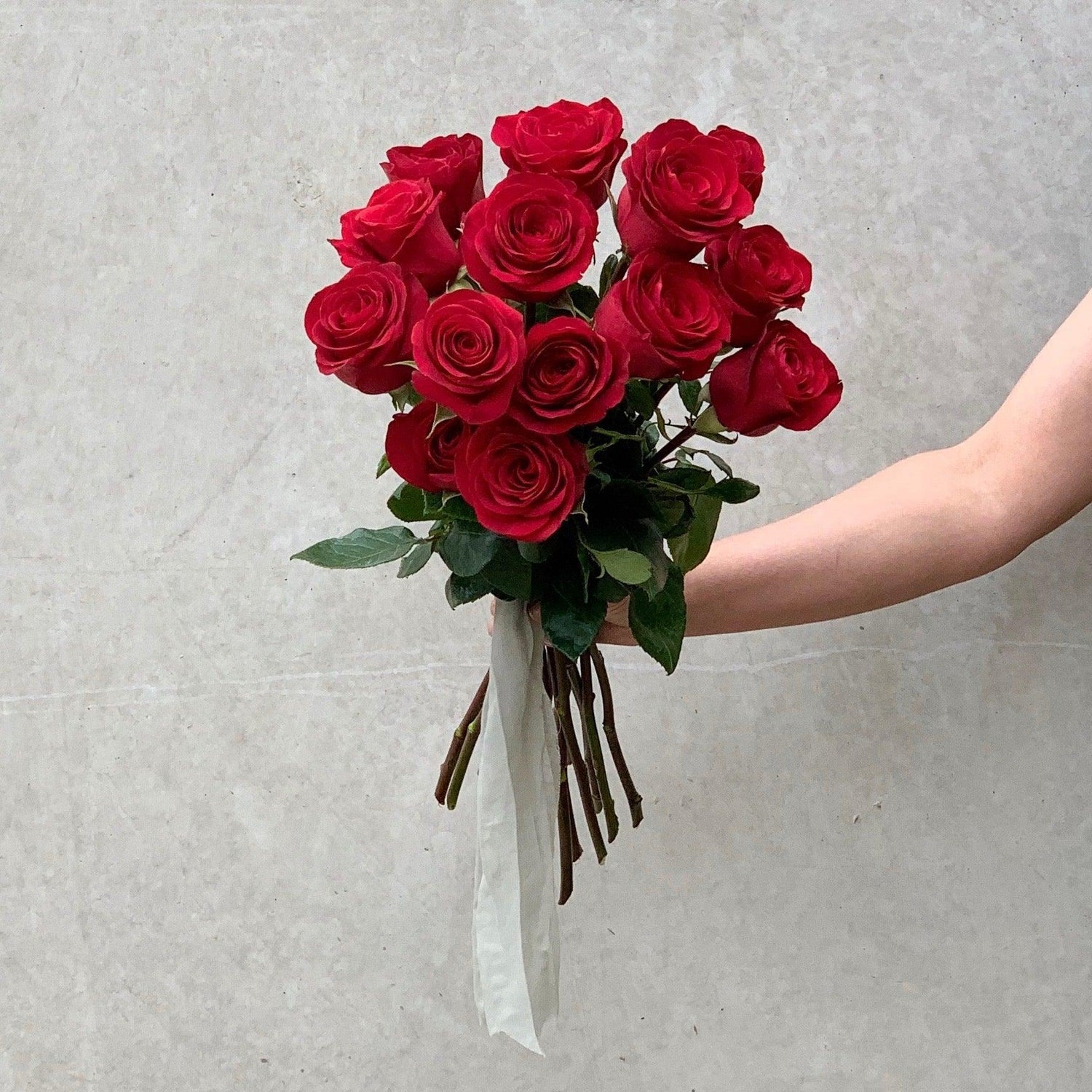 Tied bunch of one dozen roses being held by one of Herbivore's team members.