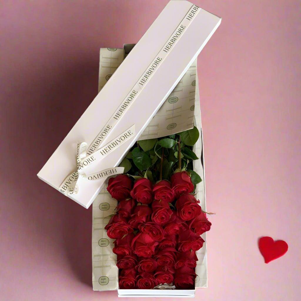 Two dozen premium long-stem red roses elegantly arranged in a signature gift box with branded wrapping.
